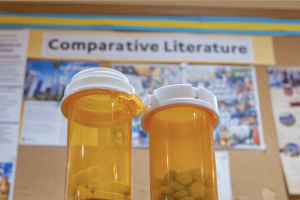 Two medication bottles are pictured in front of a comparative literature department bulletin board. UCLA will offer a health humanities minor housed under the comparative literature department starting in fall 2026. (Kai Dizon/Assistant Photo editor)