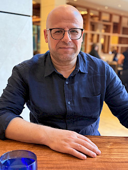 Nouri Gana sits at a table with a bookshelf in the background.